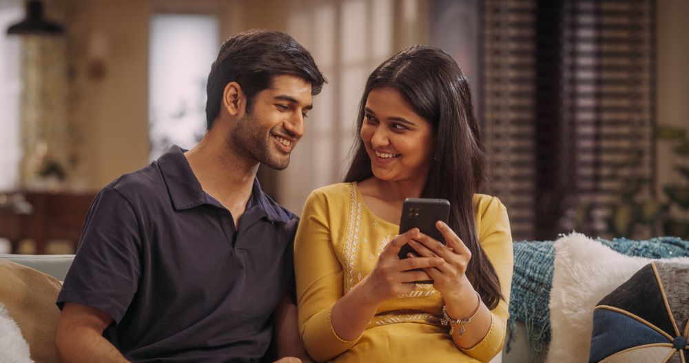 Indian Couple Using Smartphone At Home, Comparing Prices And Reviews On E-Commerce Sites.