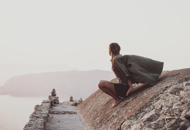 Woman sitting on castle wall looking out to sea