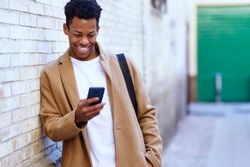 Laughing Cuban male leaning against wall looking down at his phone