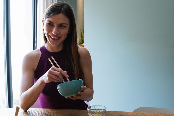 Cheerful woman with chopsticks having lunch in dining room