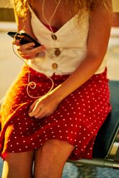 anonymous woman sitting on metal bench with earphones and smartphone