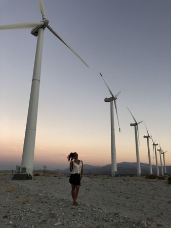 Woman standing on brown sand near wind turbines at sunset