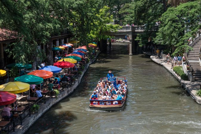 A barge loaded with visitors pass a row of colorful stalls along the San Antonio River, Texas