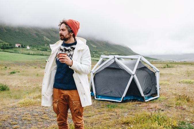 Man waking up from tent with ceramic mug on overcast day