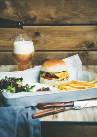 Classic hamburger with fries and beer at wooden restaurant table