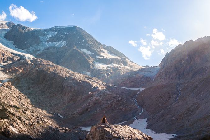 Lonely traveler sitting on peak and admiring mountains