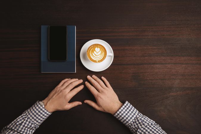 Top view of man in plaid with cappuccino, cell phone and notebook