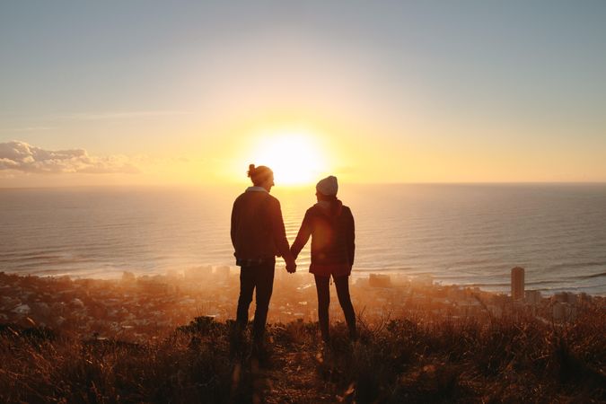 Traveling couple on cliff at sunset