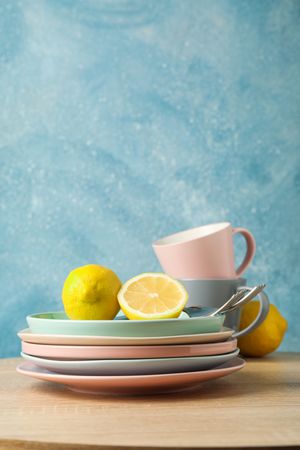 Plates and cups with lemons stacked on wooden table, space for text