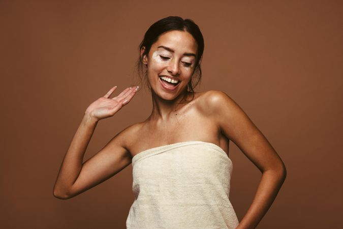 Young woman with vitiligo dancing in bath towel against brown background