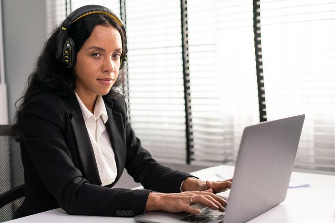 Woman wearing headphones while typing on laptop
