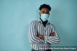 Portrait of a Black man in face mask blue studio shoot with his arms crossed 4drnA0
