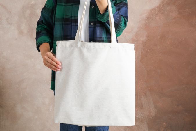 Young woman holding tote bag against brown background, empty space
