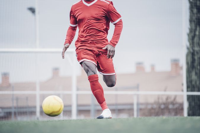 Black soccer player with red outfit playing soccer.