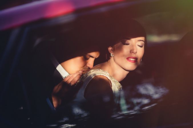 Charming bride closing eyes while groom kissing back in car