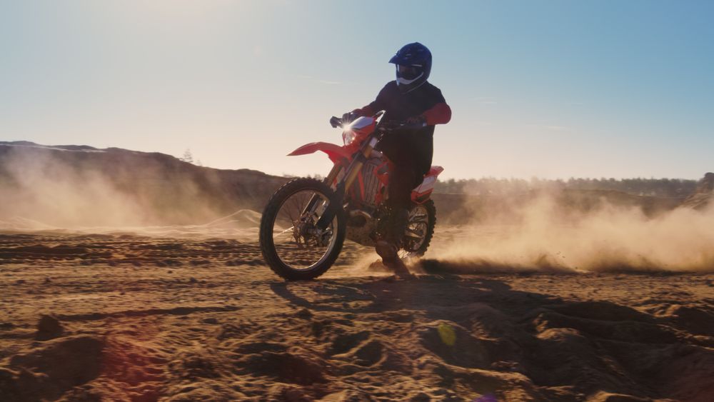 Side View Footage of the Professional Motocross Motorcycle Rider Driving on the Dune and Further Down the Off-Road Track.
