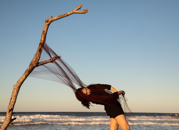 Woman in fishing net fixed on twig near water on shore