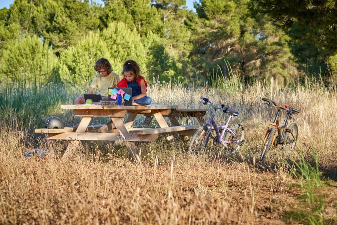 Children browsing gadgets while sitting on picnic table in count