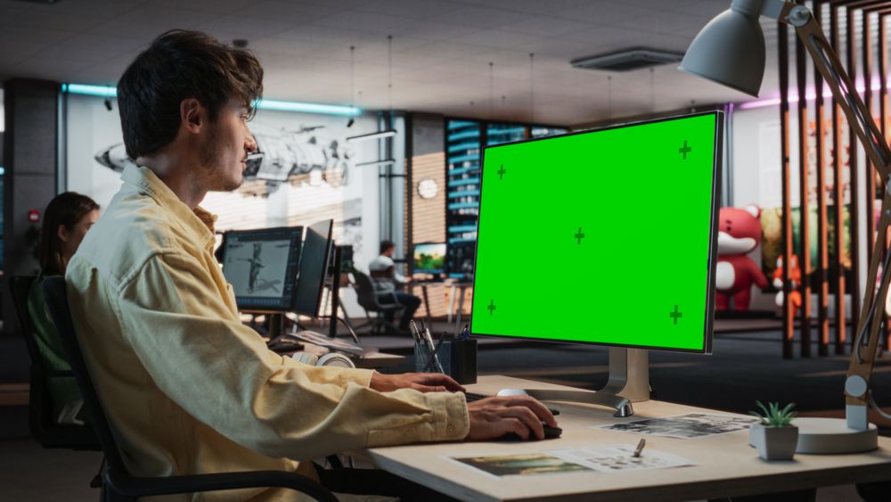 Portrait of Creative Man Sitting at a Desk Using Desktop Computer with Mock-up Green Screen Chromakey.