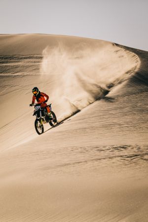 Dirt biker riding over sand dunes