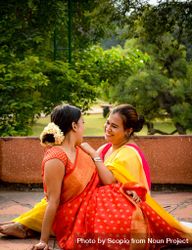 Two women in sarees sitting on green grass outdoor 0yQr70