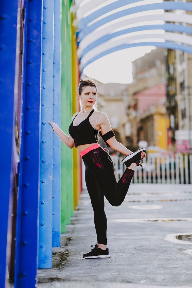 Woman with earphones stretching legs on street