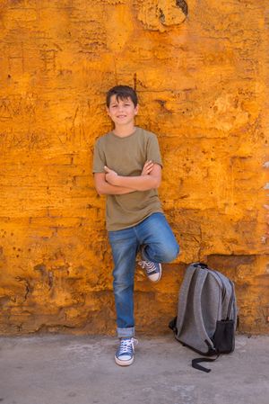 Teenage male leaning on yellow wall next to back pack