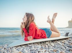 Cheerful woman lying on surfboard with crossed legs