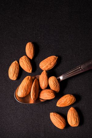 Top view of tasty almonds placed on a steel spoon on a dark background