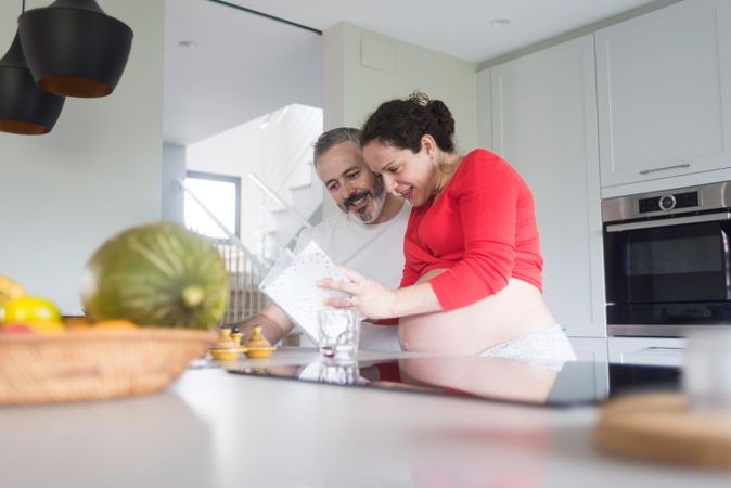 Pregnant woman and husband deciding on recipe in bright kitchen