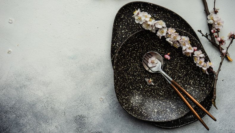 Table setting with delicate apricot blossom around elegant grey tableware with copy space