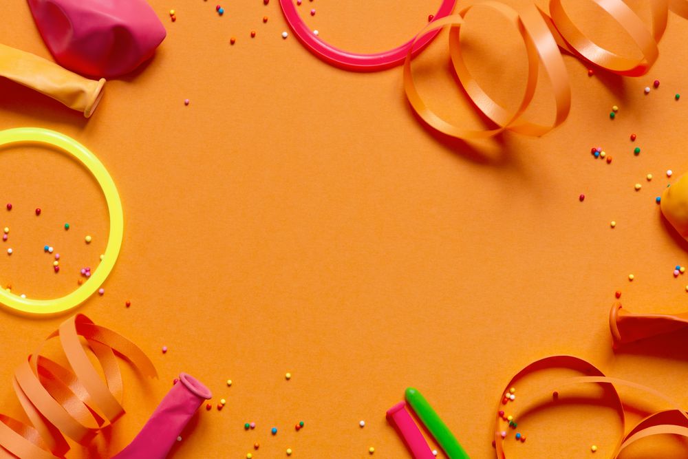 Top view of balloons, ribbons and glowing bracelets on orange background