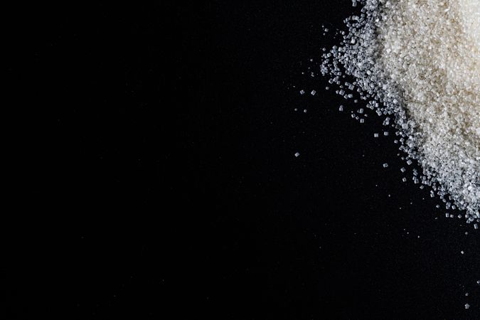 Flat lay of granulated sugar positioned on the right side over a dark background.