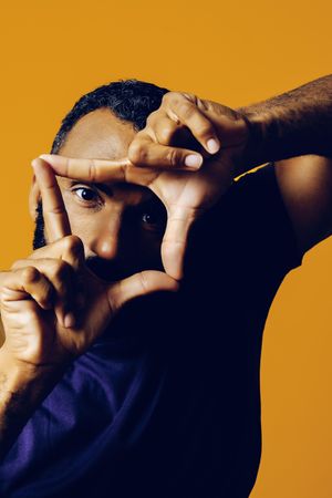 Serious Black man in yellow studio playing director with hands framing the camera