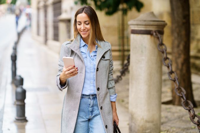 Chic woman in coat using smartphone on street