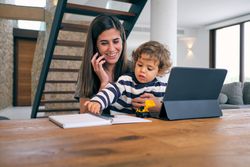 Cheerful mother talking on smartphone while sitting with baby