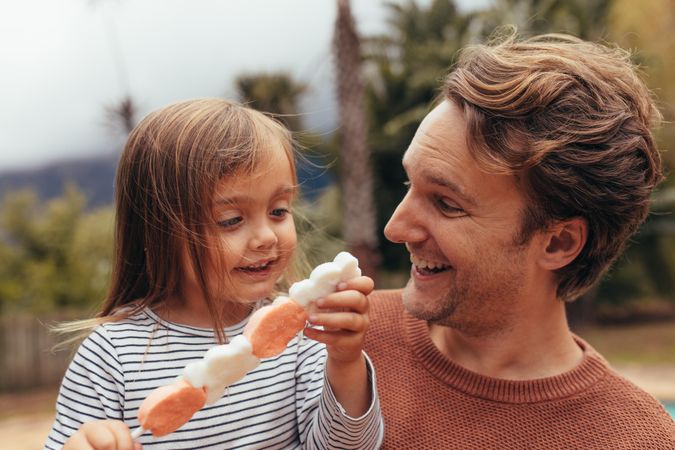 Happy daughter with her father holding a sugar candy stick outdoors