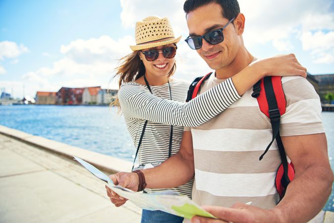 Woman with arm wrapped around boyfriend while he check maps