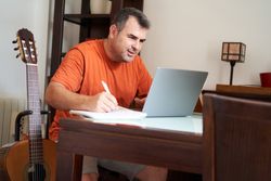 a man with a laptop computer in online guitar lessons writes scales and chords