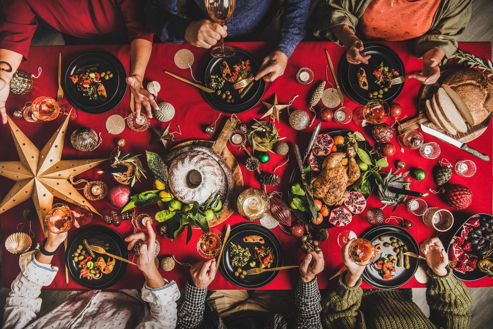 Group of people at festive red table with cake, roast chicken, decorations