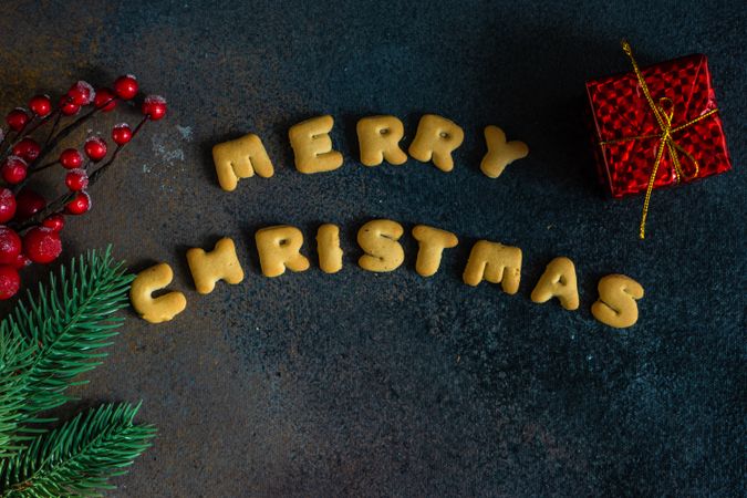 "Merry Christmas" written on dark table with red gift box and holly