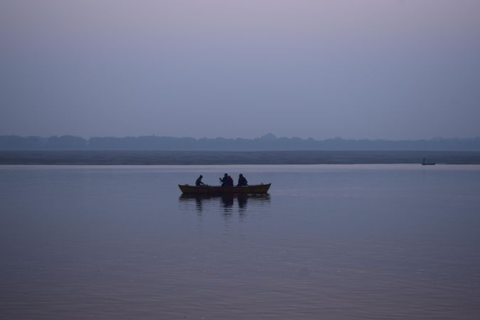 Silhouette of three people on boat on body of water during a cloudy day