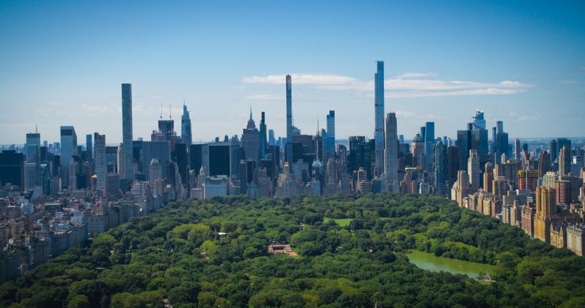 Sunny Weather New York City Aerial Landscape Over Central Park with Midtown Manhattan Skyscrapers. Cinematic Drone View of Urban Skyline with Slightly Cloudy Blue Sky