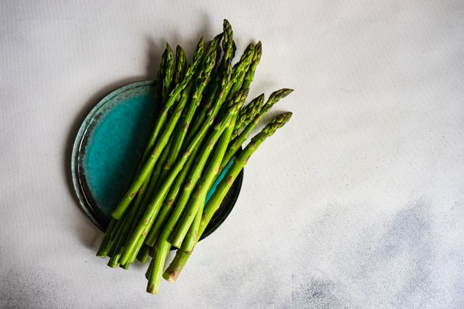 Loose raw asparagus on teal plate on marble counter with copy space