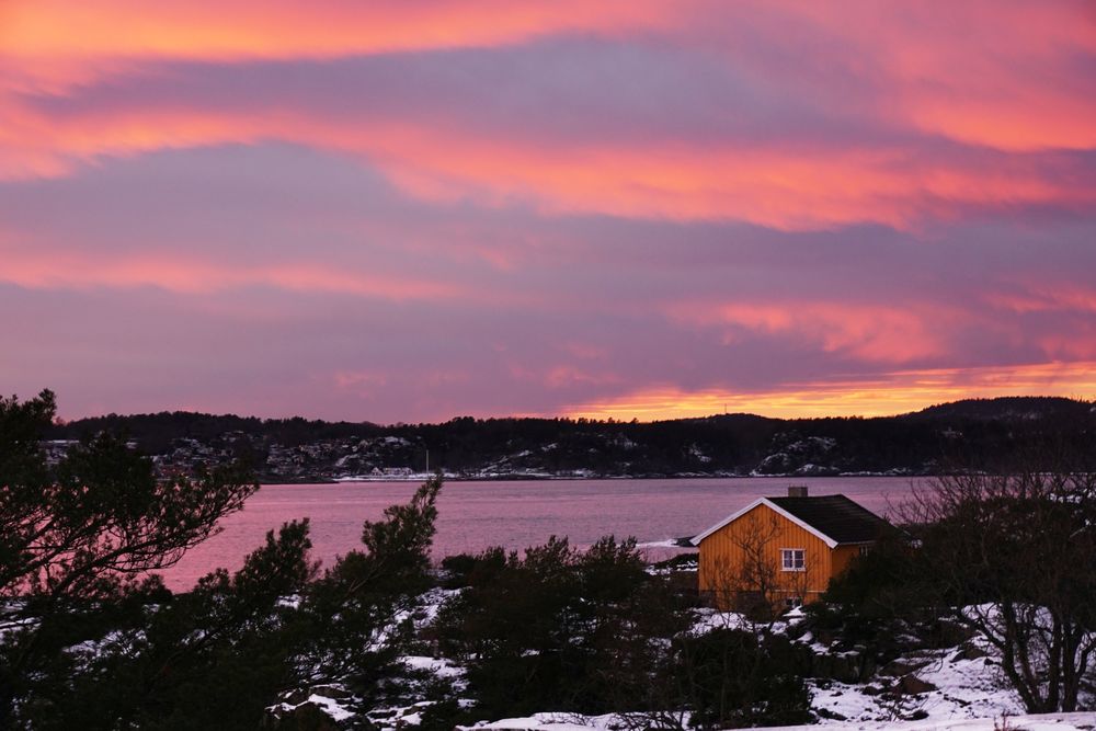 Colourful sunset over lonely house on frozen riverside
