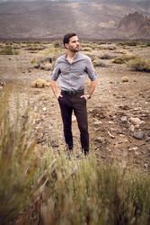 Stylish young male standing in rocky valley with savanna grass