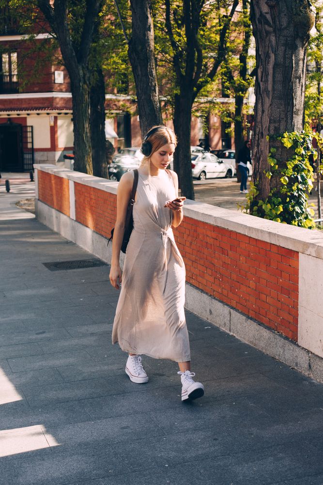 Young woman with headphones and smartphone walking outdoors