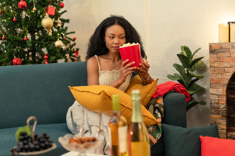 Black woman sitting on a sofa and holding a bucket of popcorn