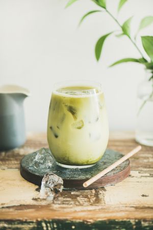 Close up of iced matcha drink with creamer on side, with eco friendly straw and leaves