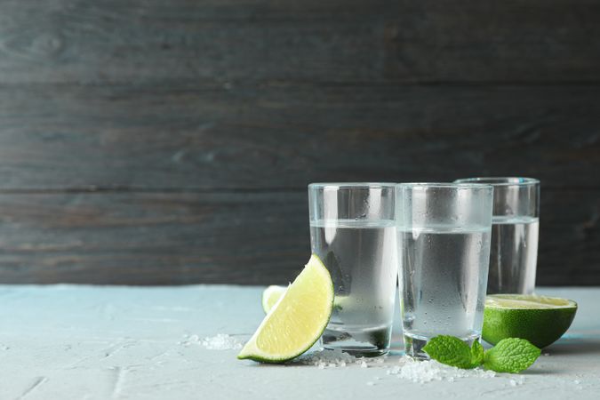 Tequila shots, salt, lime slices and mint on table against wooden background
